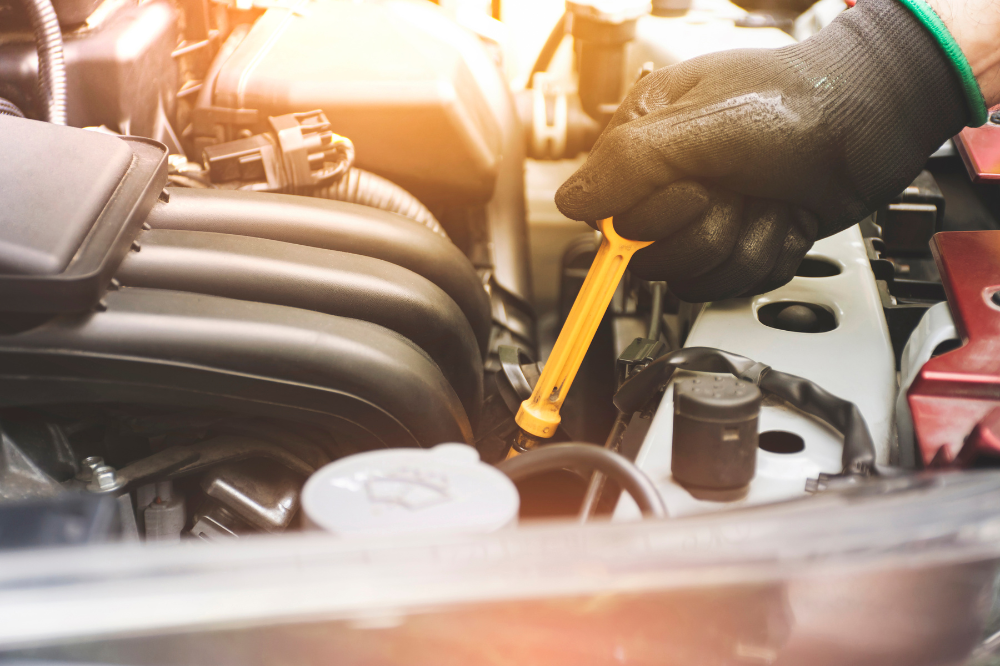 car maintenance, Auto Repair & Service, Auto Body Repair & Auto Collision Repair in McAllen, Edinburg & Harlingen, TX. Gloved hand pulling out the oil dipstick from a car engine during a routine oil check in a brightly lit garage.