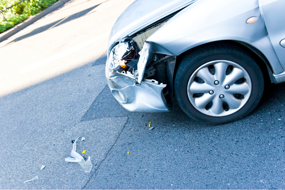 fender bender, Auto Repair & Service, Auto Body Repair & Auto Collision Repair in McAllen, Edinburg & Harlingen, TX. Close-up of a silver car with significant front-end collision damage and broken headlight components scattered on the road.