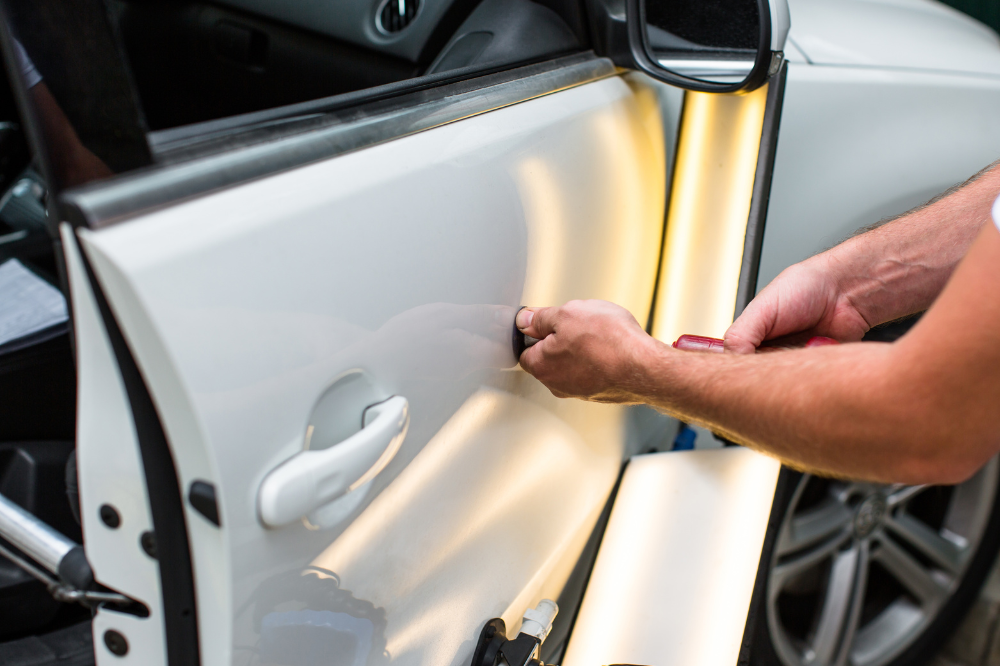 Paintless Dent Repair in Harlingen, TX by Premium Collision. A technician performing paintless dent repair on a white car door using specialized tools and lighting to remove a small dent.