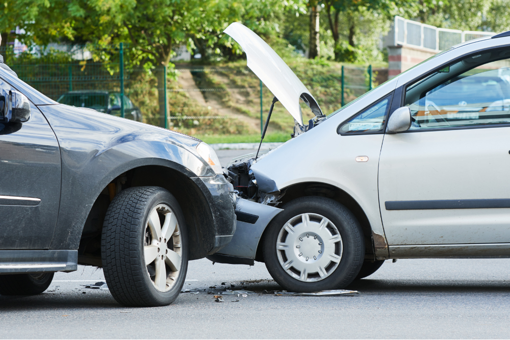 Collision Repair Harlingen, TX by Premium Collision. Two cars involved in a front-end collision on a roadway, with the front of the silver car damaged and its hood open, and debris scattered on the ground.
