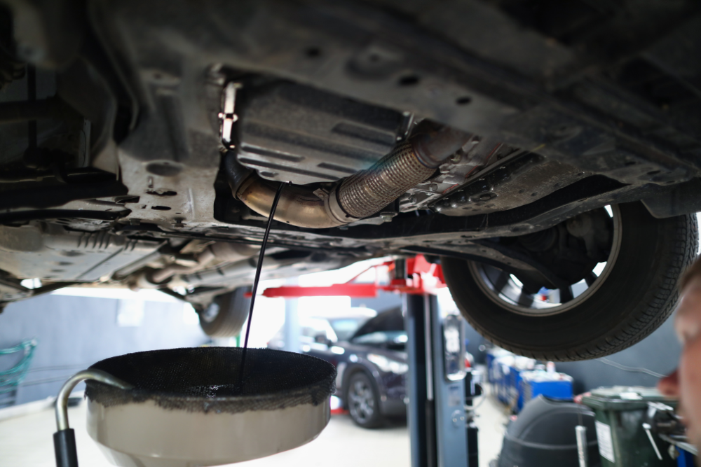 Preventive Maintenance in Edinburg, TX by Premium Automotive. View from beneath a raised vehicle as engine oil drains into a collection pan in an auto repair shop.