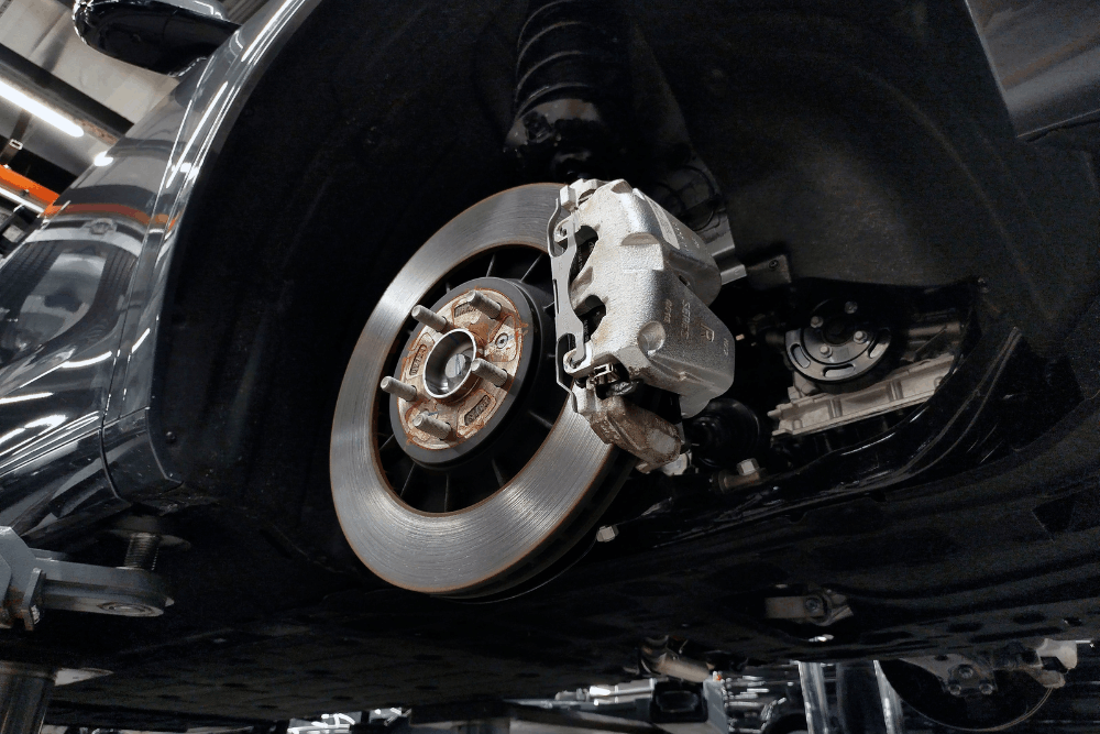 Brake repair in McAllen, TX by Premium Automotive. Image of a vehicle on a lift with the wheel removed, showing the brake rotor, caliper, and suspension components, highlighting professional brake inspection and repair for safe stopping performance.
