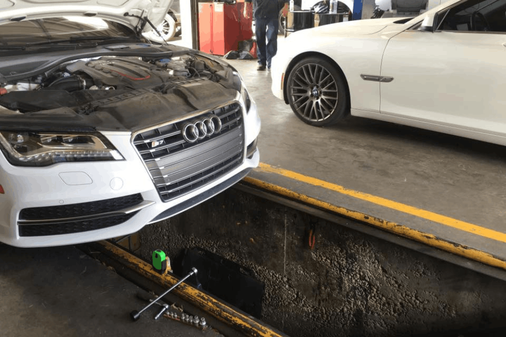 Car care, auto repair in Edinburg, TX by Premium Automotive. Image of an Audi with the hood open positioned over a service pit inside a professional auto repair shop, showing engine inspection and routine vehicle maintenance focused on performance, safety, and reliability.