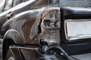 Collision parts, collision repair in Harlingen, TX at Premium Collision. Image of a damaged rear corner with a broken taillight, scraped body panel, and cracked bumper needing repair.
