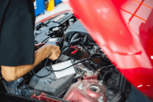 Vehicle inspection, auto repair in Edinburg, TX at Premium Automotive. Image of a technician testing a car battery under the hood of a red vehicle to support reliable vehicle maintenance.