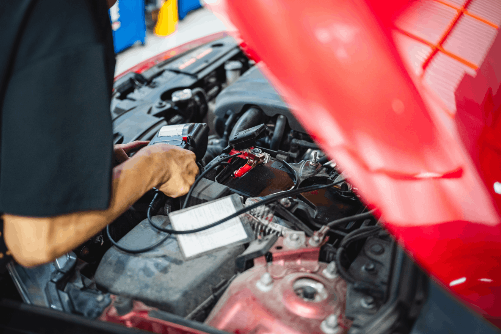 Vehicle inspection, auto repair in Edinburg, TX at Premium Automotive. Image of a technician testing a car battery under the hood of a red vehicle to support reliable vehicle maintenance.