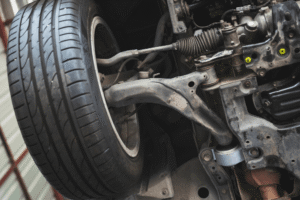 Suspension damage, auto repair in Edinburg, TX at Premium Automotive. Image of a vehicle undercarriage showing the control arm, steering rack, tie rod, and wheel assembly during inspection and service.