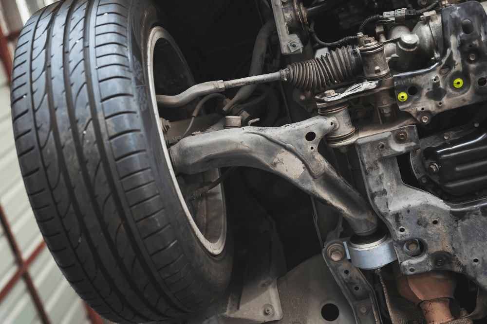Suspension damage, auto repair in Edinburg, TX at Premium Automotive. Image of a vehicle undercarriage showing the control arm, steering rack, tie rod, and wheel assembly during inspection and service.